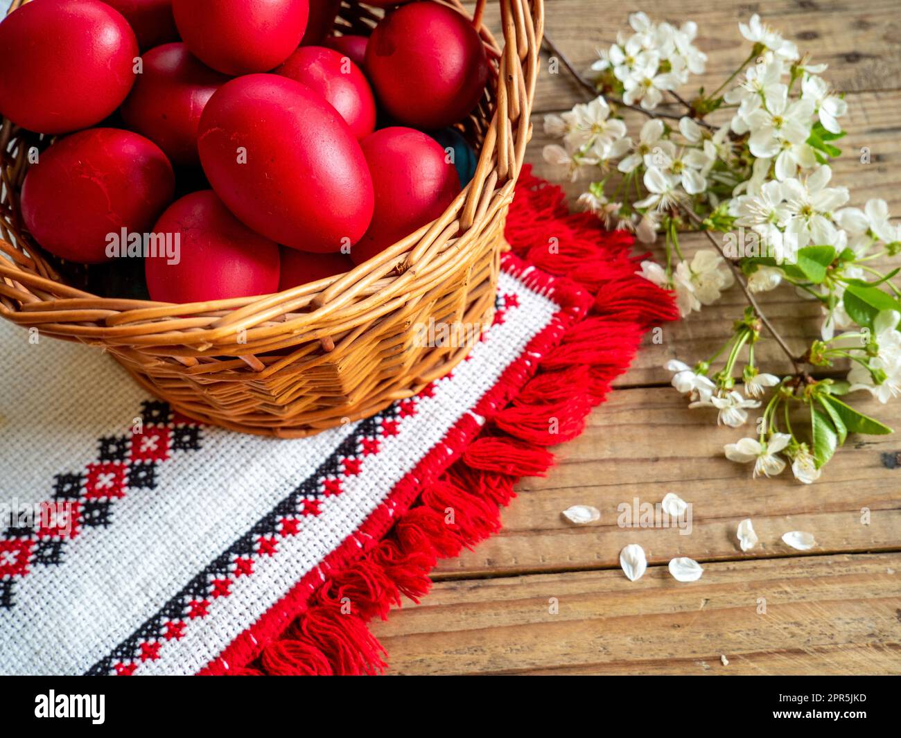 basket of red Easter eggs next to flowering branches on wooden table Stock Photo