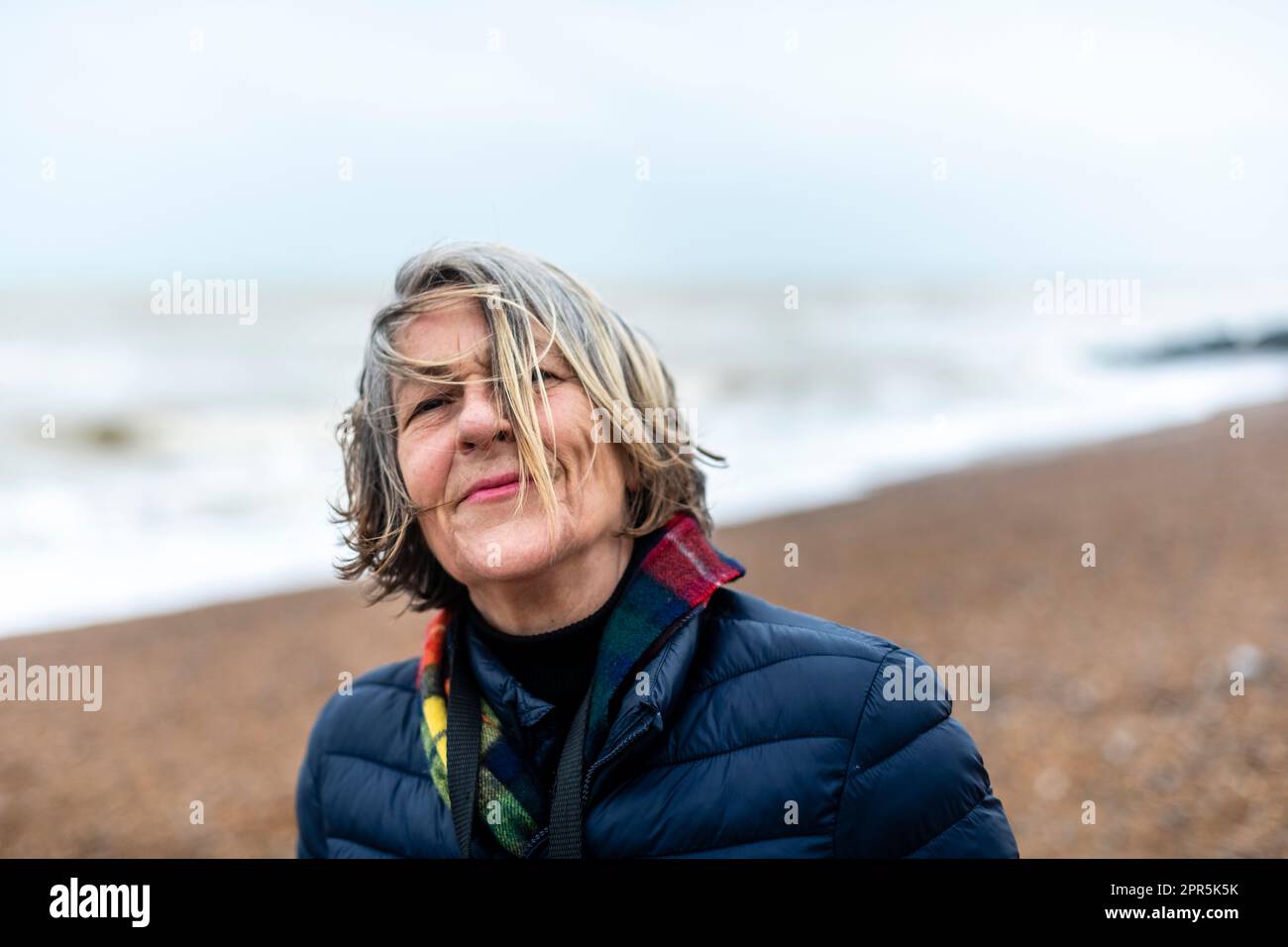 Middle age woman Wind swept on the beach looking at camera smiling Stock Photo
