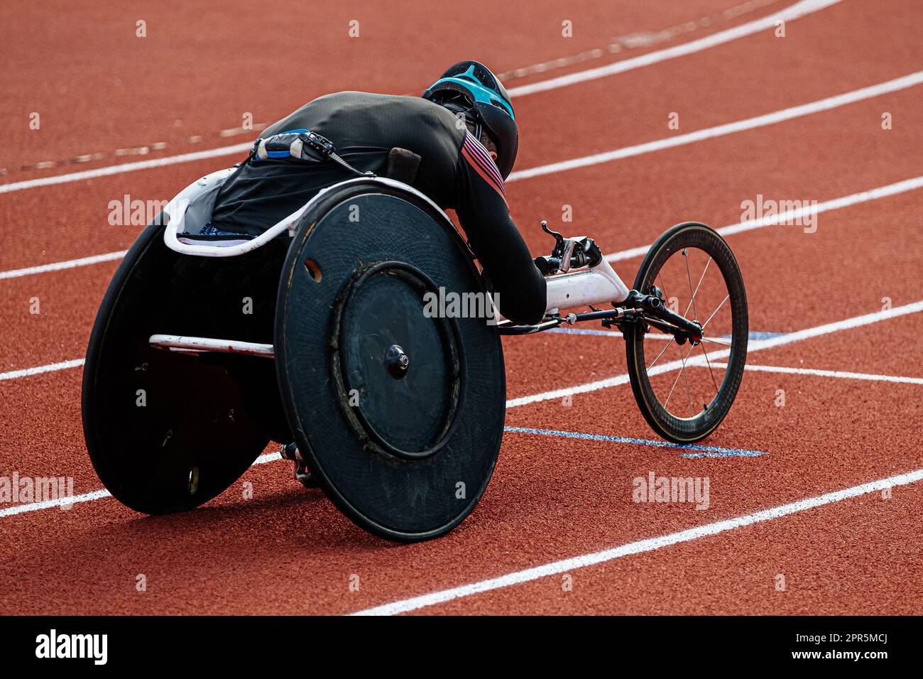 rear view para athlete in wheelchair racing riding on red track stadium, summer para athletics championships Stock Photo