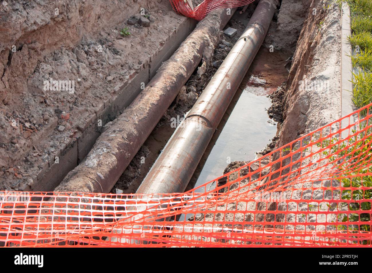 Repair of the heating plant system with the laying of new underground metal pipes in the trench. Reconstruction of the city heating system. Mesh fencing for work safety Stock Photo