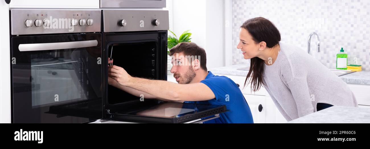 Technician In Overall Fixing Oven In Kitchen Stock Photo