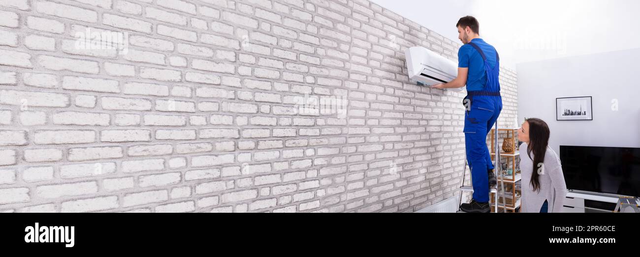 Male Technician Fixing Air Conditioner On Wall Stock Photo