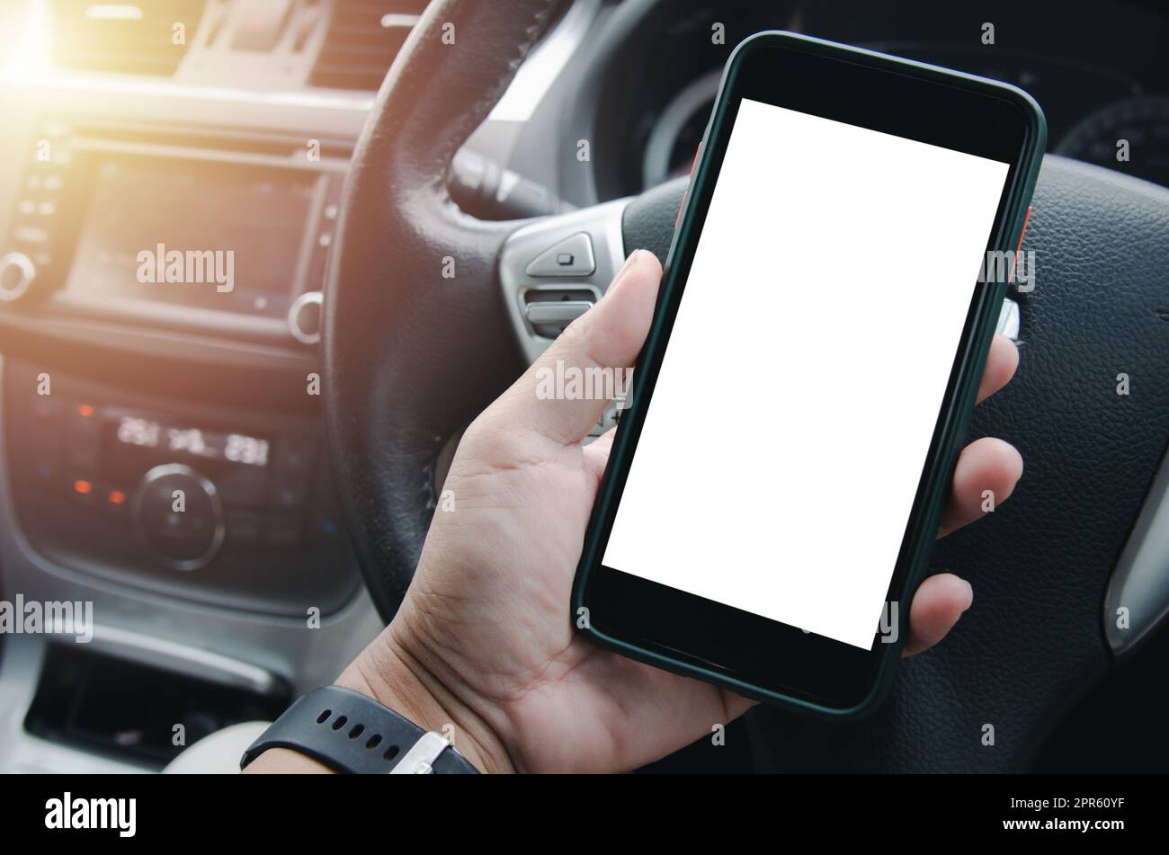 male hand holding a mobile phone in the car cabin.Blank with white screen.Mock up smart phone interior car. Stock Photo