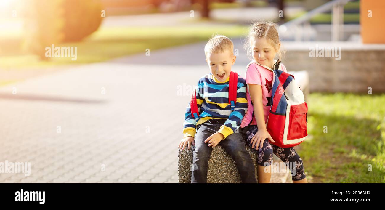 Boy and girl sitting on the stone near the school Stock Photo