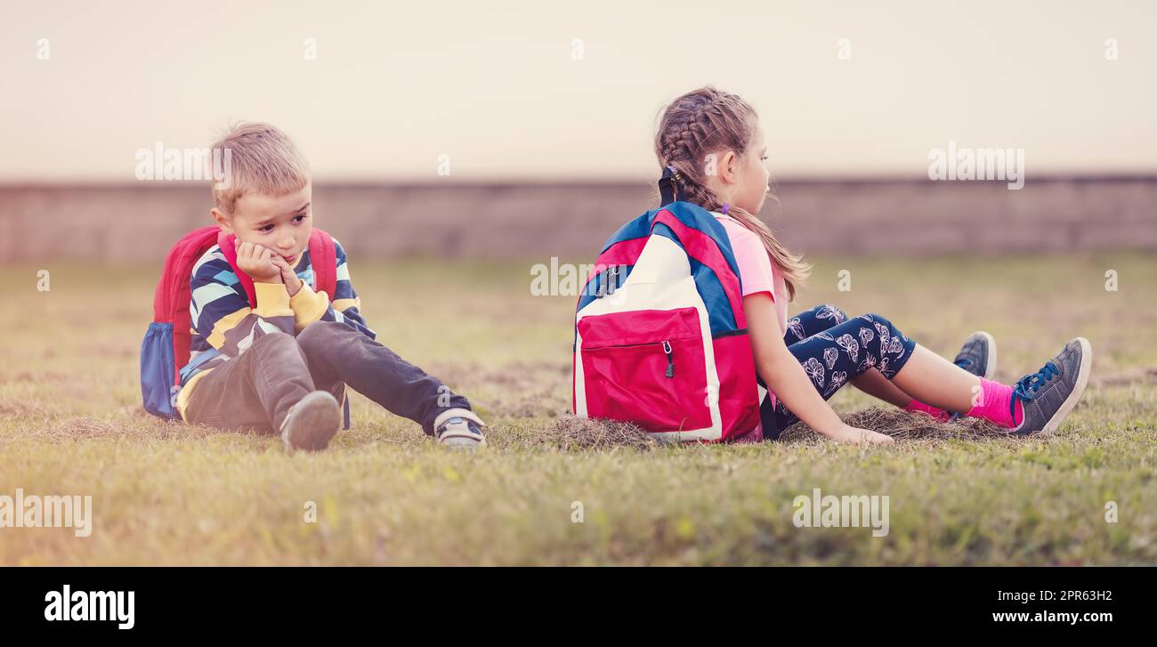 A boy and a girl quarreling and are sitting on the grass in the schoolyard back to back Stock Photo