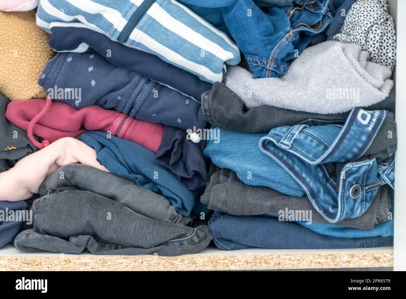 Chaotic wardrobe and sloppy closet shows many outfits of a woman with shopping addiction and many clothes like pullovers, shirts and trousers as crumpled laundry stored into a messy heap of fashion Stock Photo