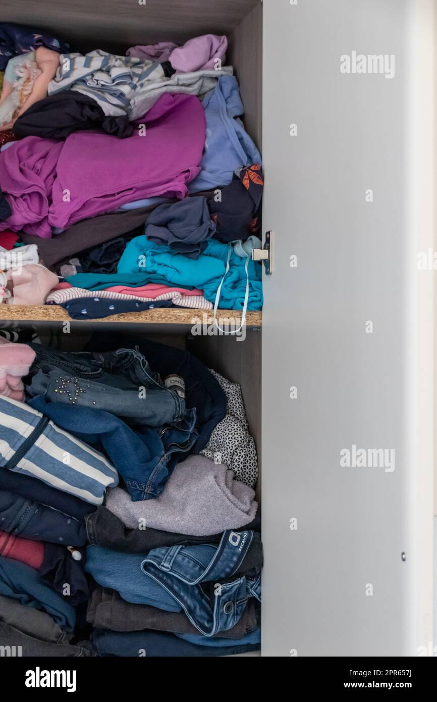 Chaotic wardrobe and sloppy closet shows many outfits of a woman with shopping addiction and many clothes like pullovers, shirts and trousers as crumpled laundry stored into a messy heap of fashion Stock Photo