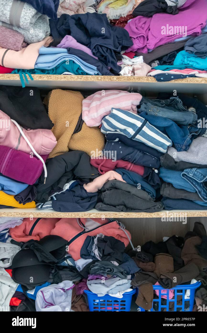 Chaotic wardrobe and sloppy closet shows many outfits of a woman with shopping addiction and many clothes like pullovers, shirts and trousers as crumpled laundry stored into a messy heap of fashion Stock Photo