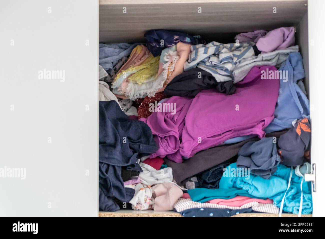 Chaotic wardrobe and sloppy closet shows many outfits of a woman with shopping addiction and many clothes like pullovers, shirts and trousers as crumpled laundry stored into a messy heap of fashion Stock Photo