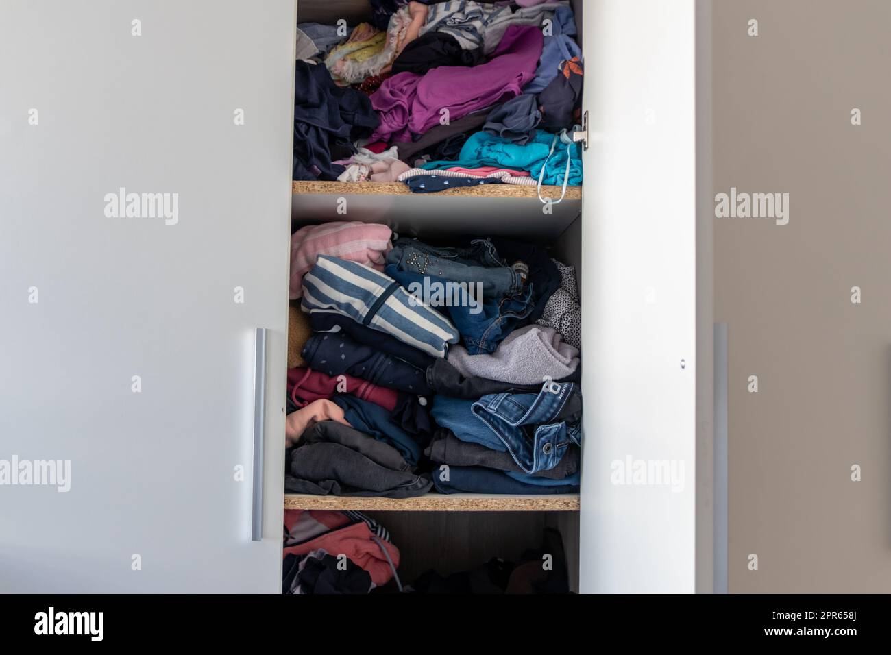 Chaotic wardrobe and sloppy closet shows many outfits of a woman with shopping addiction and many clothes like pullovers, shirts and trousers as crumpled laundry stored into a messy heap of fashion Stock Photo