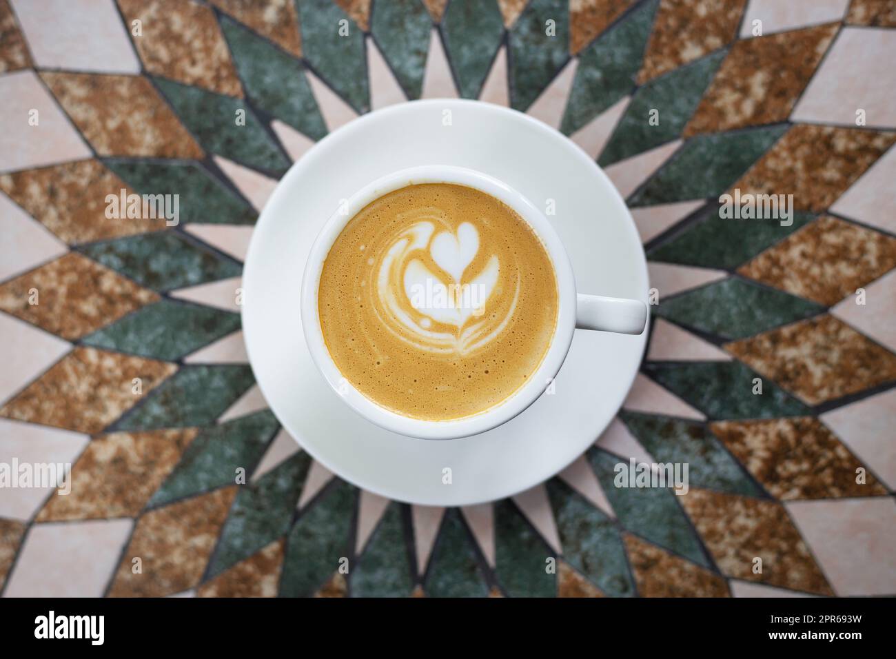 White cup of cappuccino coffee with heart-shaped foam on a beautiful table. View from above. Stock Photo