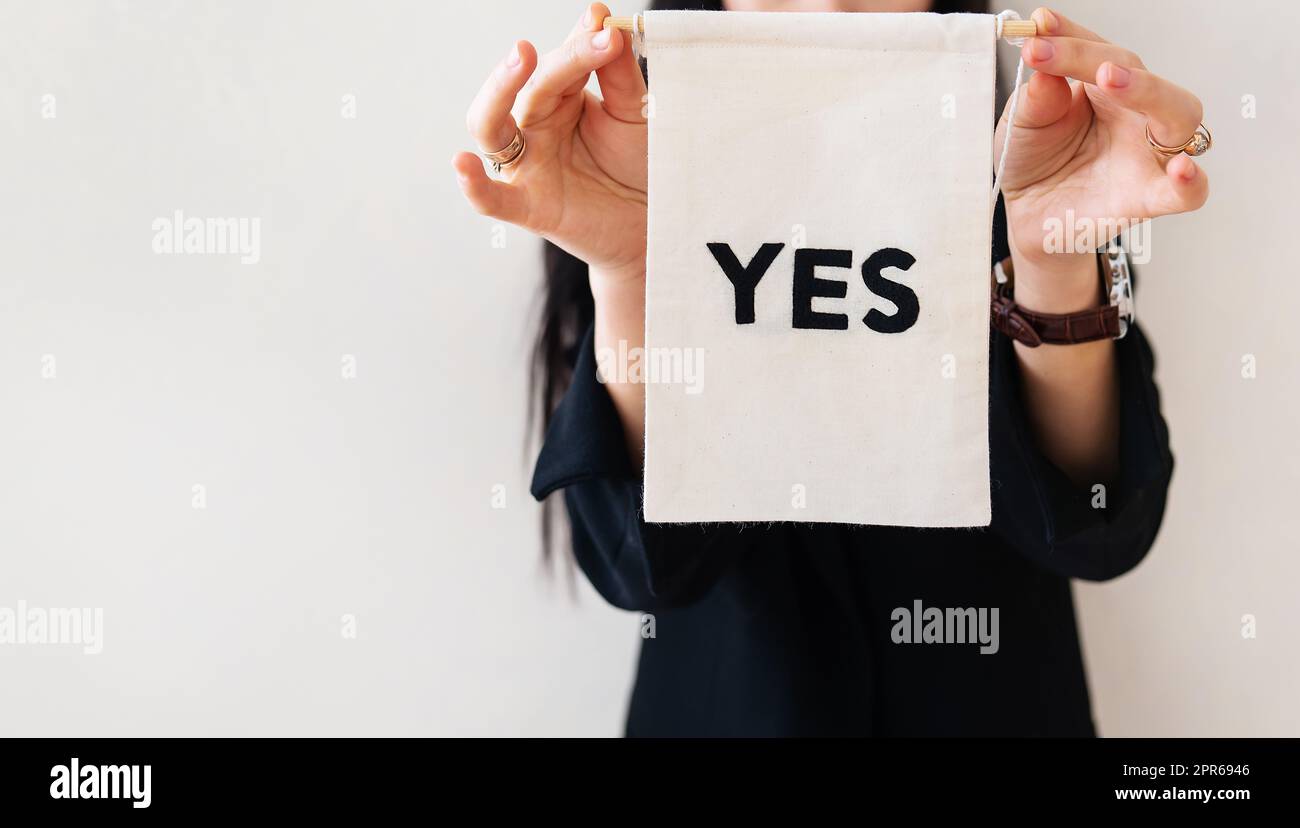 Young business woman in a black suit shows a blank white billboard on a white isolated background. The poster says yes. Concept for business and advertising. Banner. Stock Photo