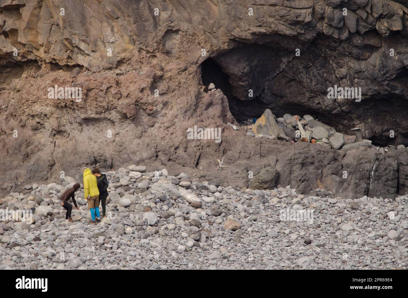 Three people talking and one doing yoga in a cave on the right. Stock Photo
