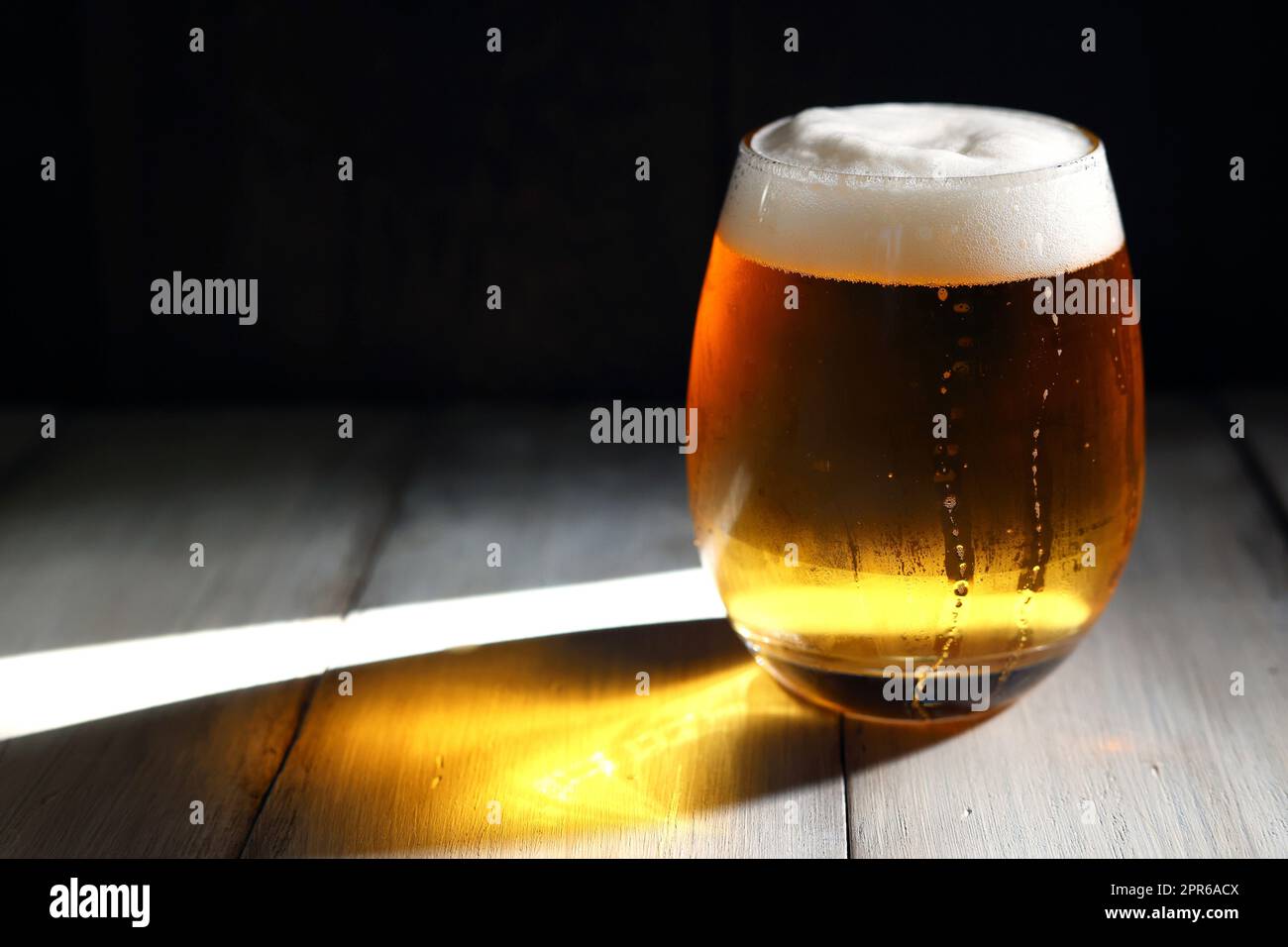 A frothy beer poured into a short, rounded glass illuminated by the strong afternoon light Stock Photo