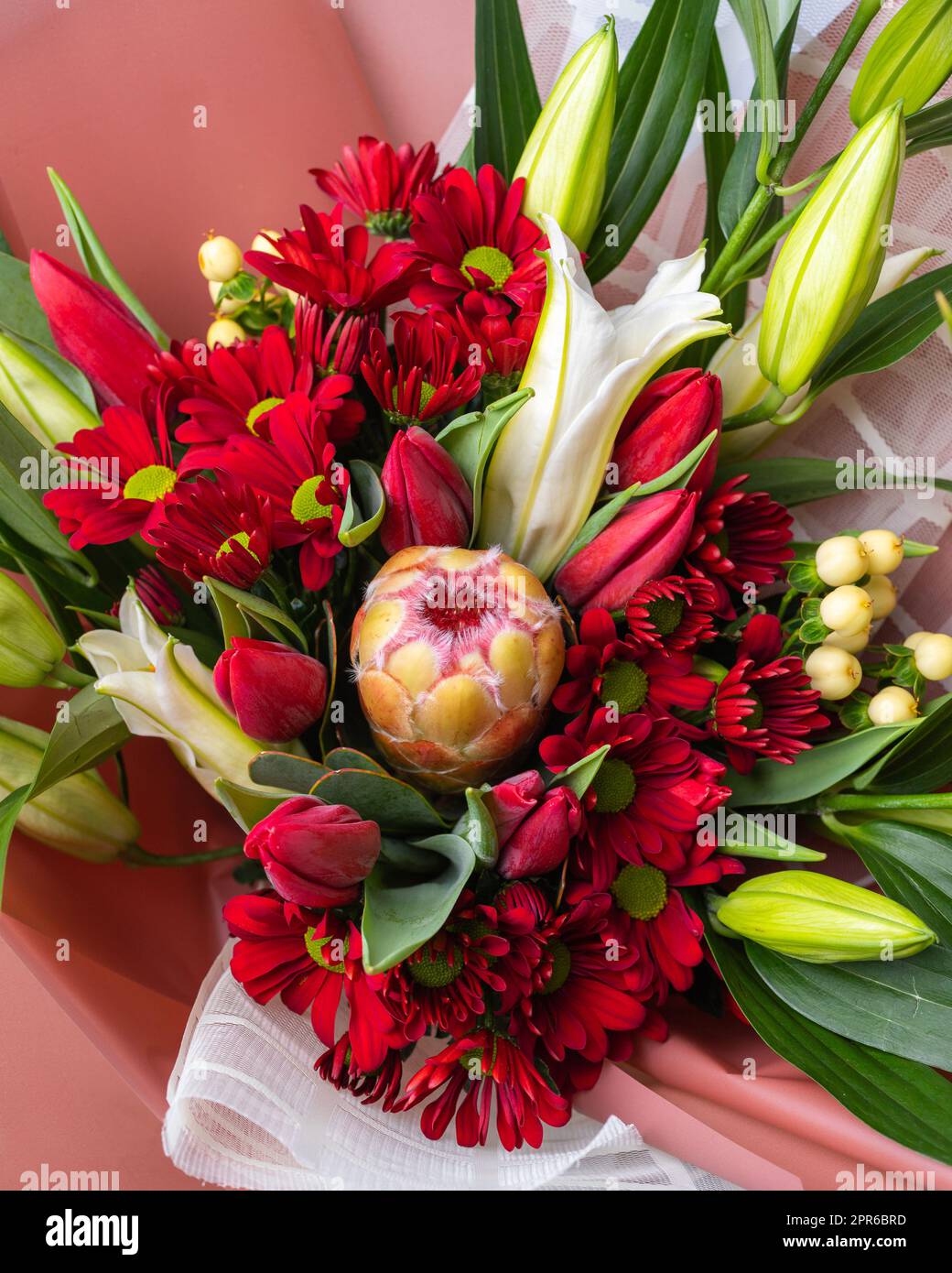 Close up top view of bouquet of bright flowers in red and green colors wrapped in paper. Stock Photo