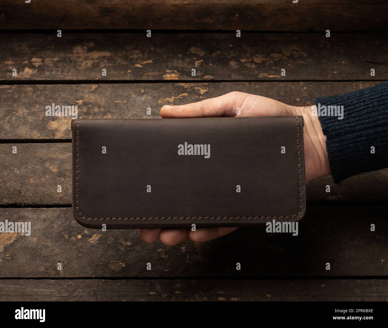 Leather men's wallet in a man's hand on a vintage wooden background Stock Photo