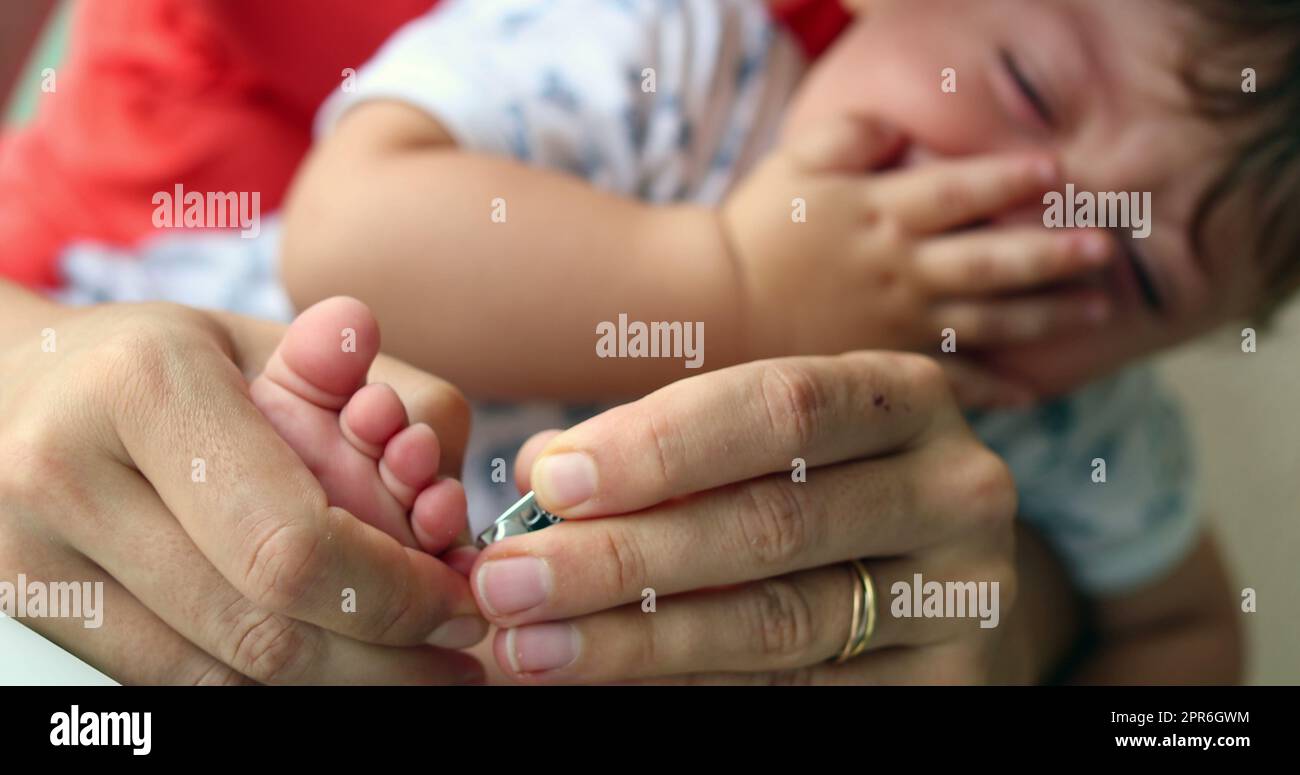 Mother trimming crying baby nails. Parent cutting clipping infant toddler son while complaining Stock Photo