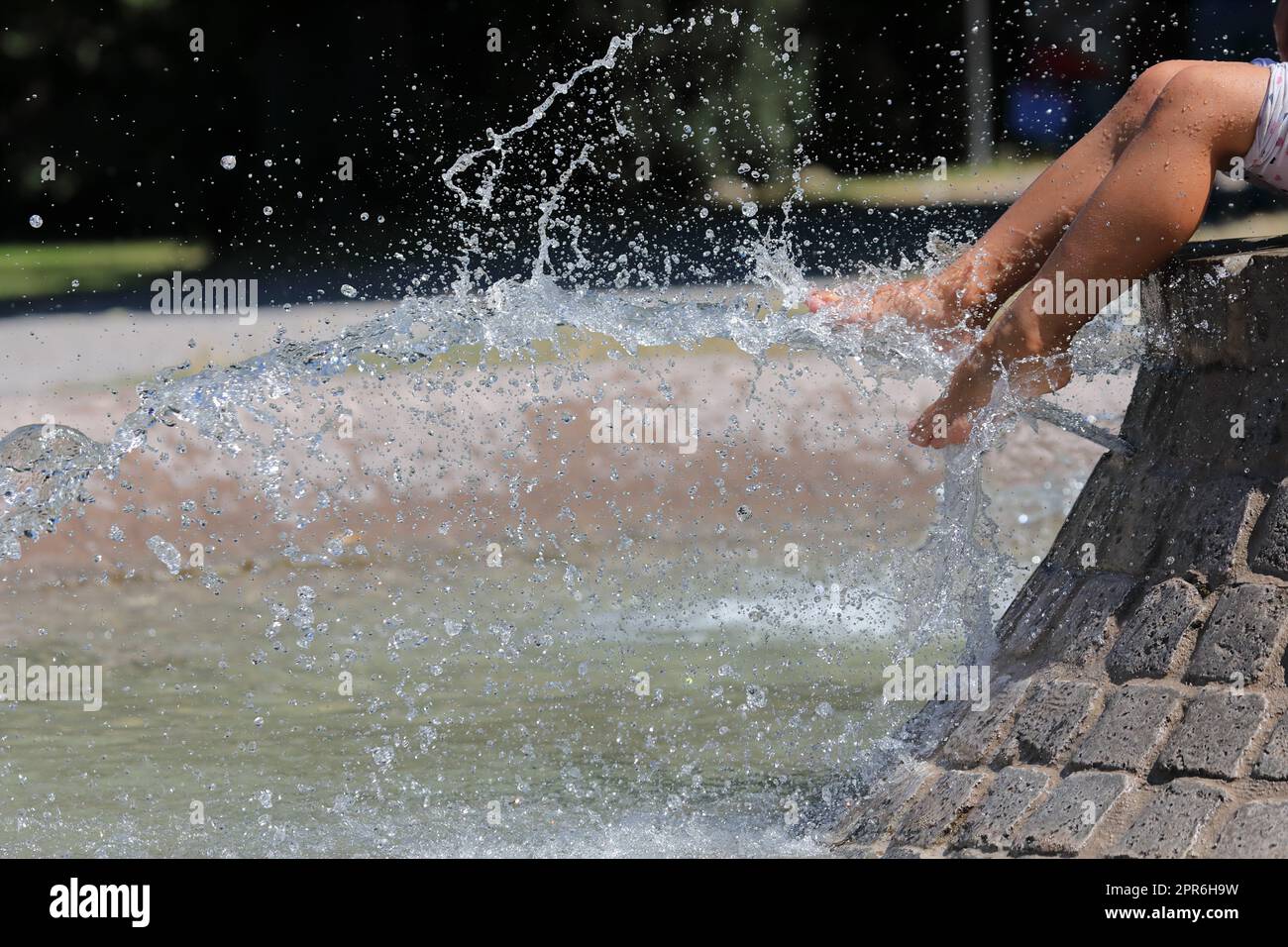 Beautiful legs of a girl sitting on a city fountain. Selective focus