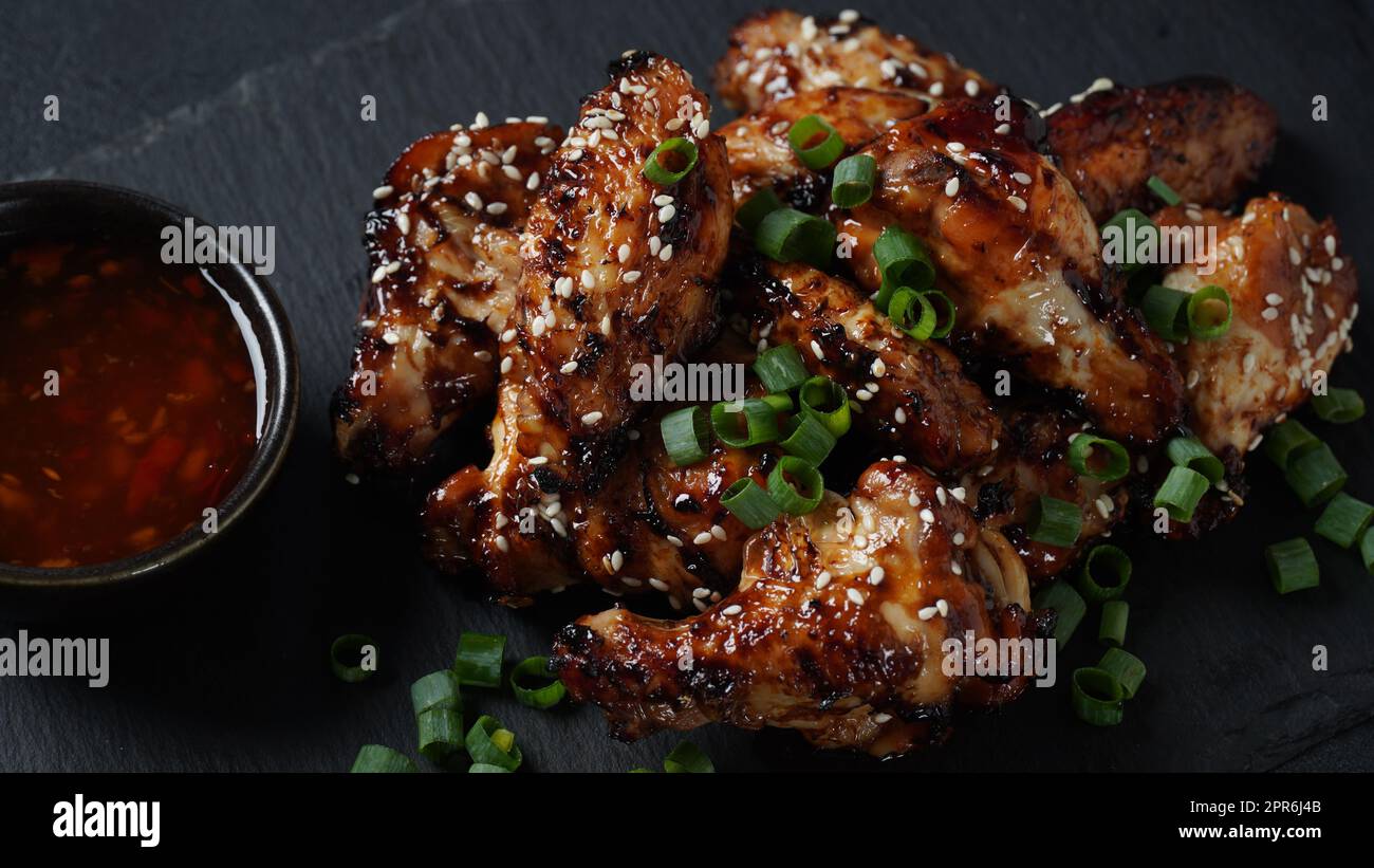 Grilled chicken wings with sauce garnished with green onions on slate