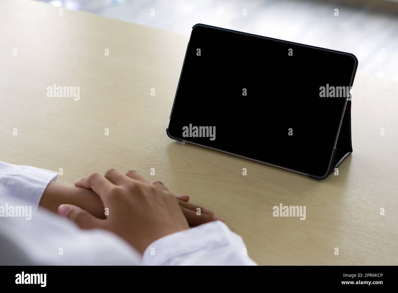 Back view of woman in white gown using a blank screen tablet while sitting at the wooden table. Stock Photo