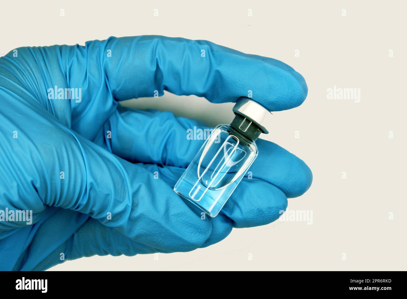 A hand in a blue medical glove close-up holding a vaccine against a light background. The concept of the fight against Covid19. Stock Photo
