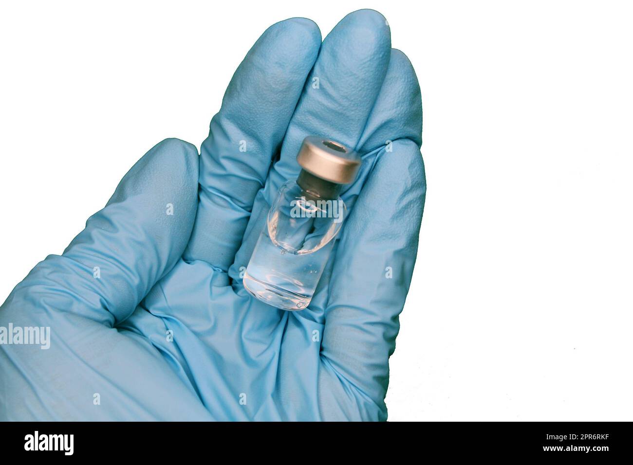 A hand in a blue medical glove close-up holding a vaccine against a light background. The concept of the fight against Covid19. Stock Photo