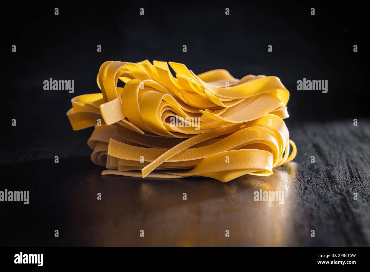 Uncooked pappardelle pasta on black table. Stock Photo