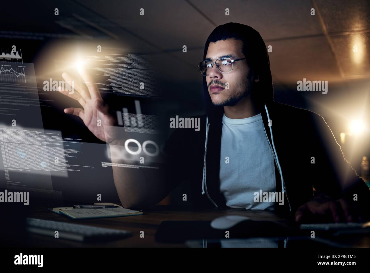 Hacking is a skill that comes second-nature to him. Shot of a young hacker cracking a computer code in the dark. Stock Photo