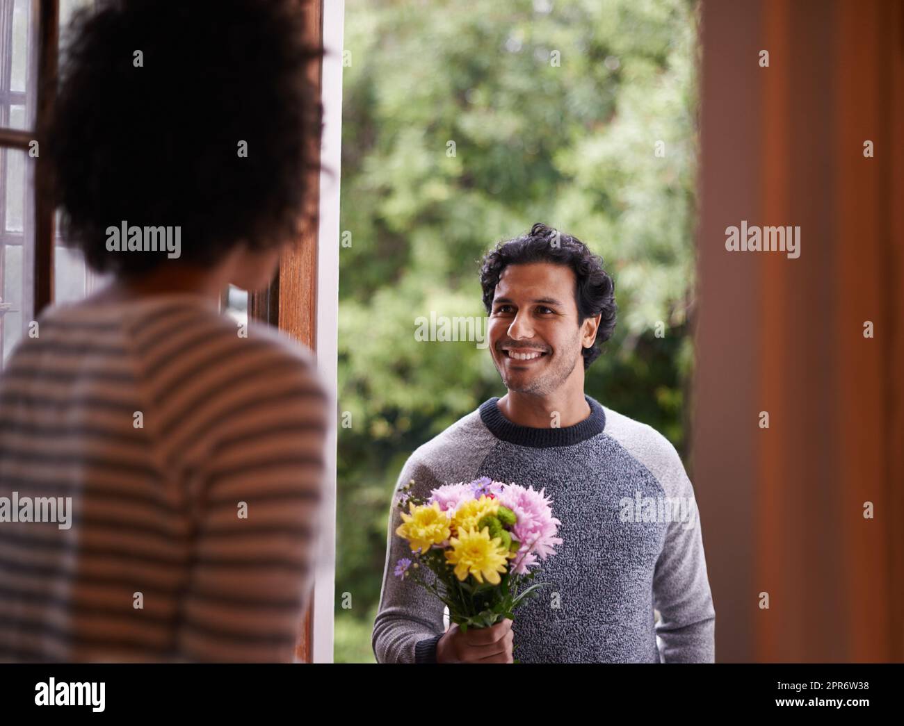 For you...my love. Cropped shot of a young man surprising his wife with flowers. Stock Photo