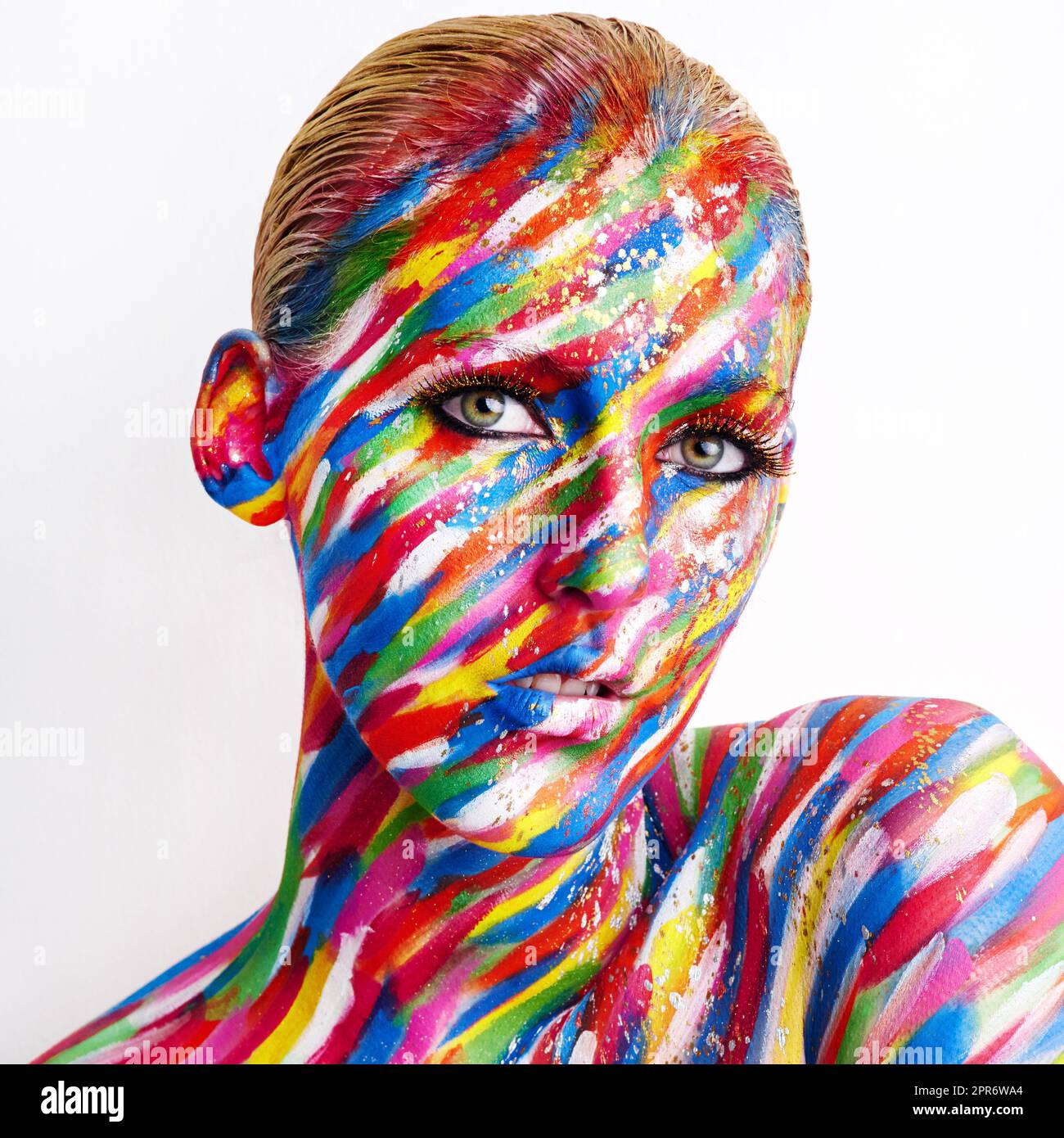 Bold is beautiful. Studio shot of a young woman posing with brightly colored paint on her face against a white background. Stock Photo