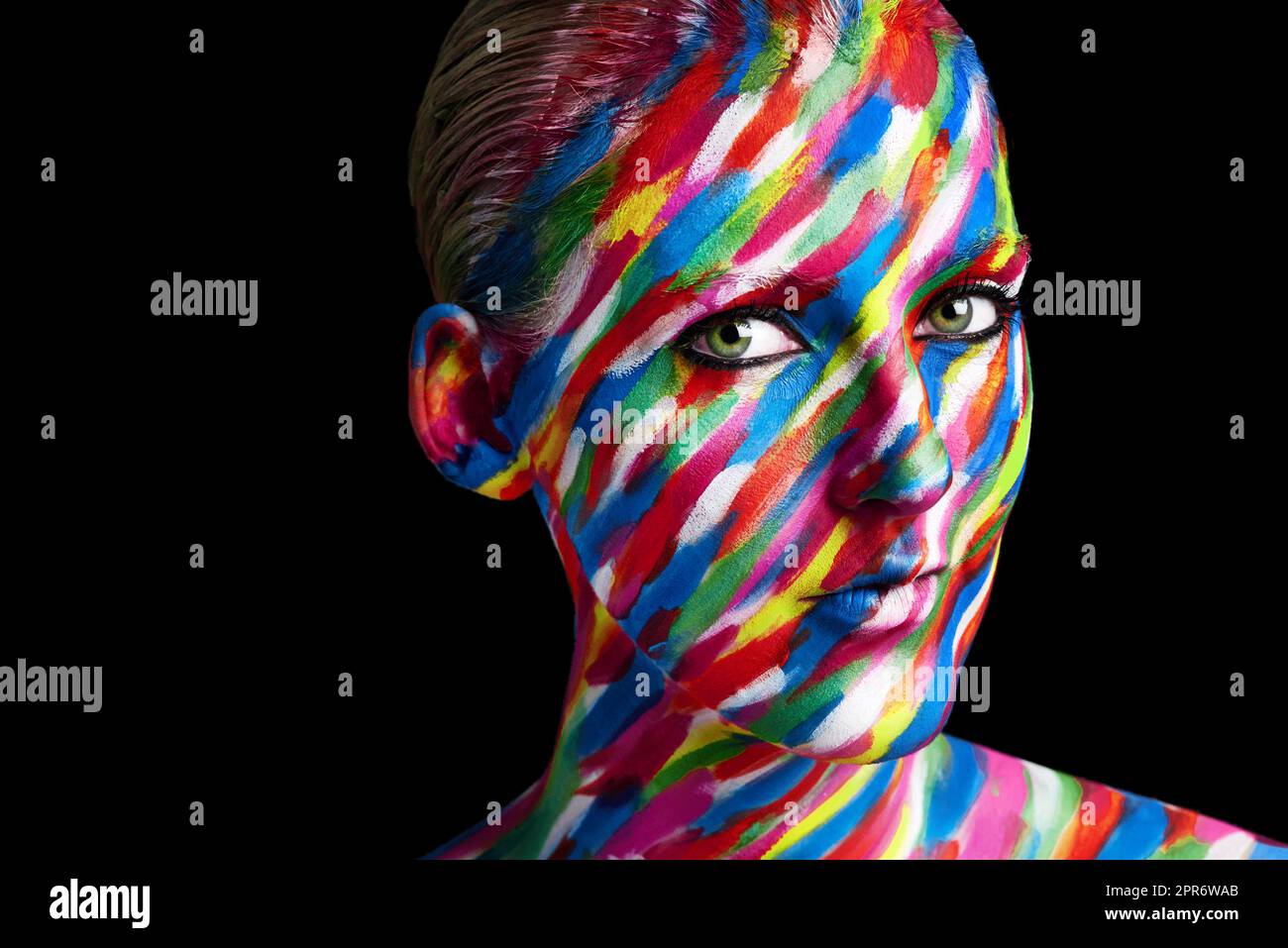 Getting creative with colors. Studio shot of a young woman posing with brightly colored paint on her face against a black background. Stock Photo