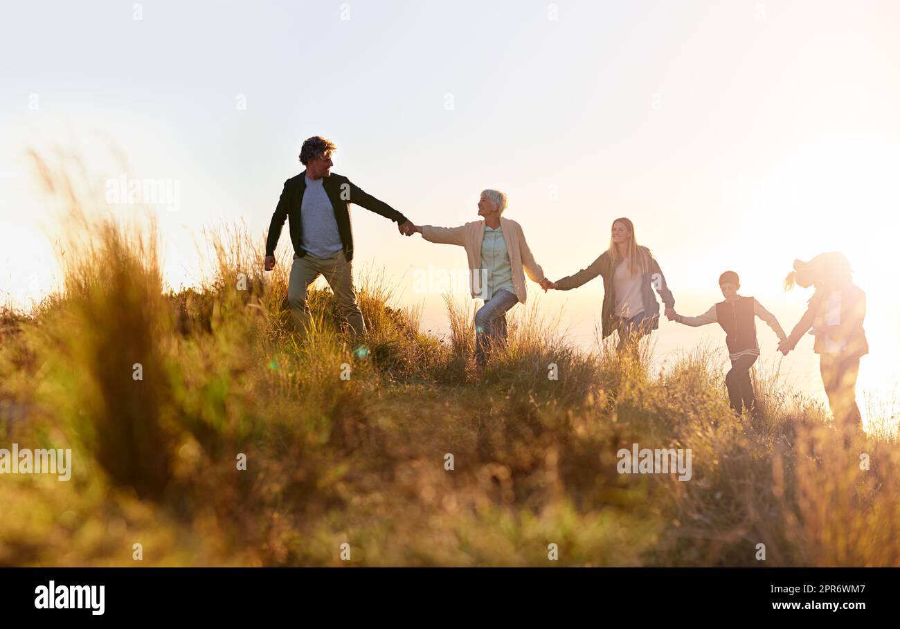 Grandpa is in the lead. Shot of a multi-generational family walking hand in hand across a field at sunset. Stock Photo