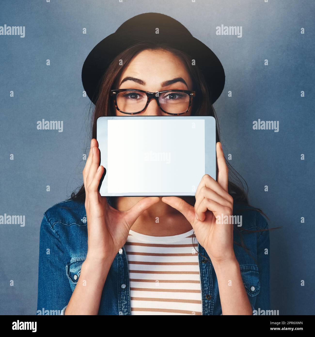 Have I got the app for you. Shot of an attractive young woman holding tablet in front of her face in studio. Stock Photo