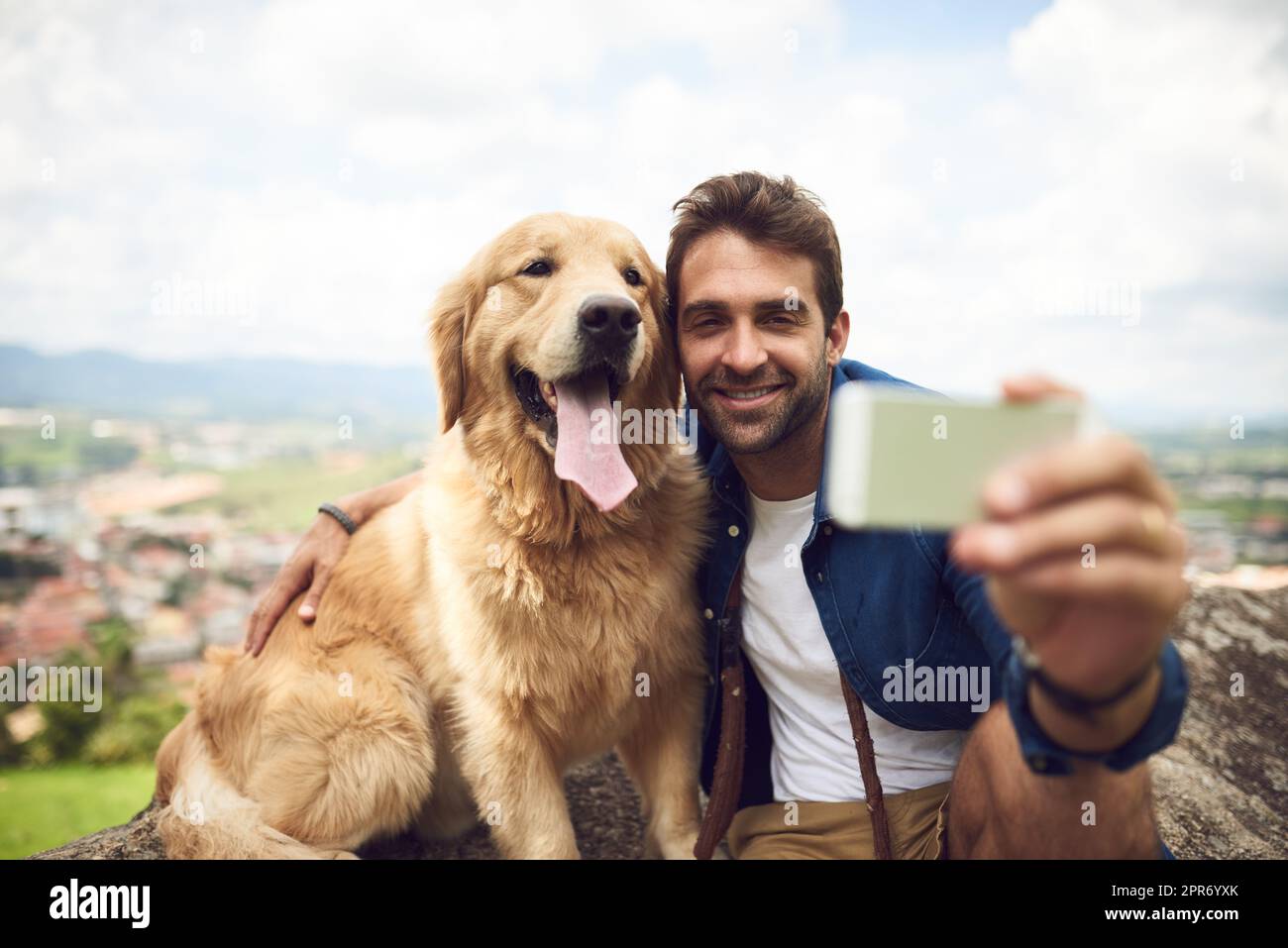 Just one more from the top. Full length shot of a handsome young man and his dog taking selfies while resting during a hike in the mountains. Stock Photo