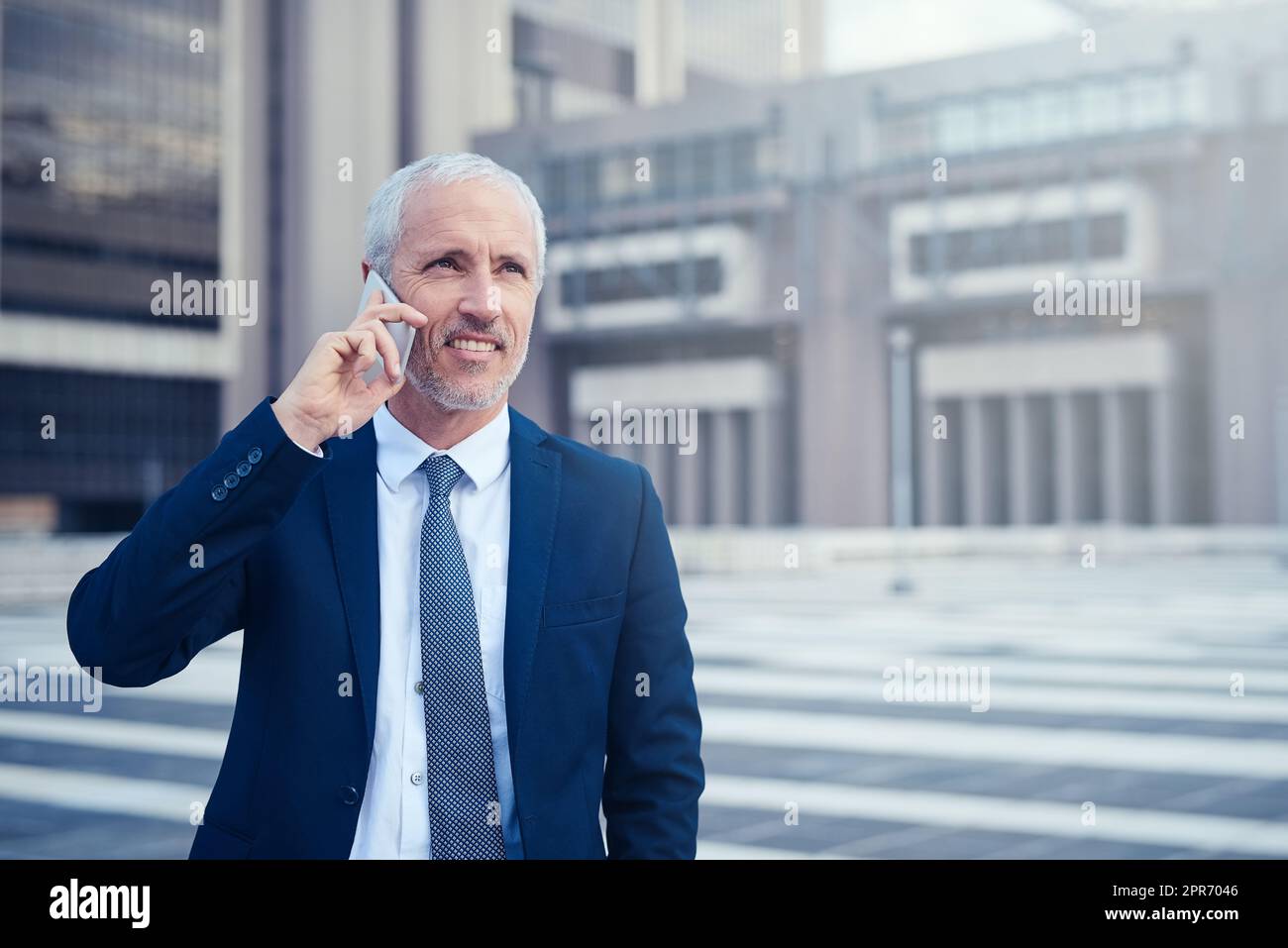 Ive been expecting your call. Shot of a businessman answering his phone while walking to his office in the city. Stock Photo