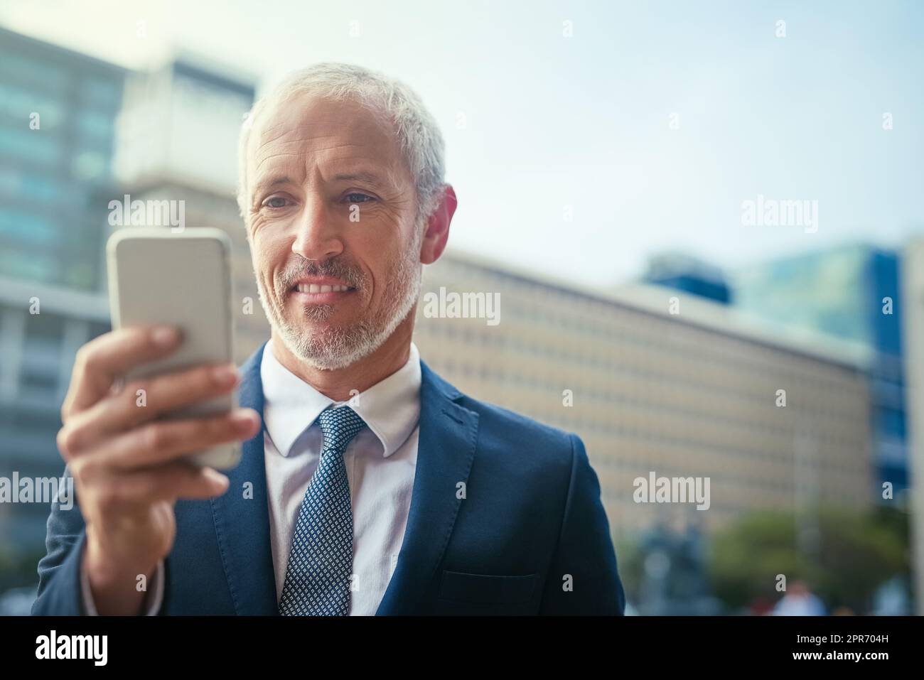 Letting his fingers do the talking. Shot of a confident businessman using his cellphone while standing outside his office building. Stock Photo