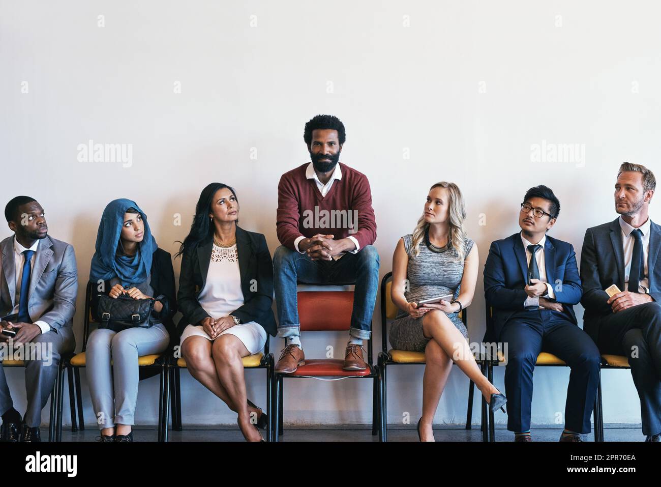He is certain he will make the cut. Shot of a group of confident businesspeople waiting in line for their interviews while a man sits on top of a chair inside of a office during the day. Stock Photo