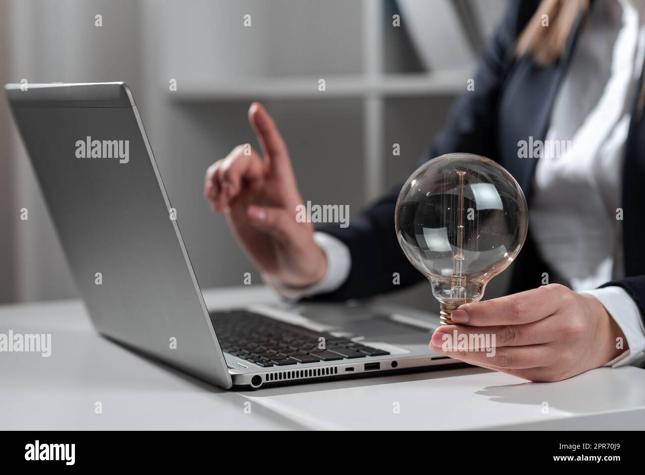 Businesswoman Pointing Recent Updates With One Finger On Desk Holding Lightbulb. Woman In Office Showing Important Message On Computer. Executive Presenting Crutial Data Into Pc. Stock Photo
