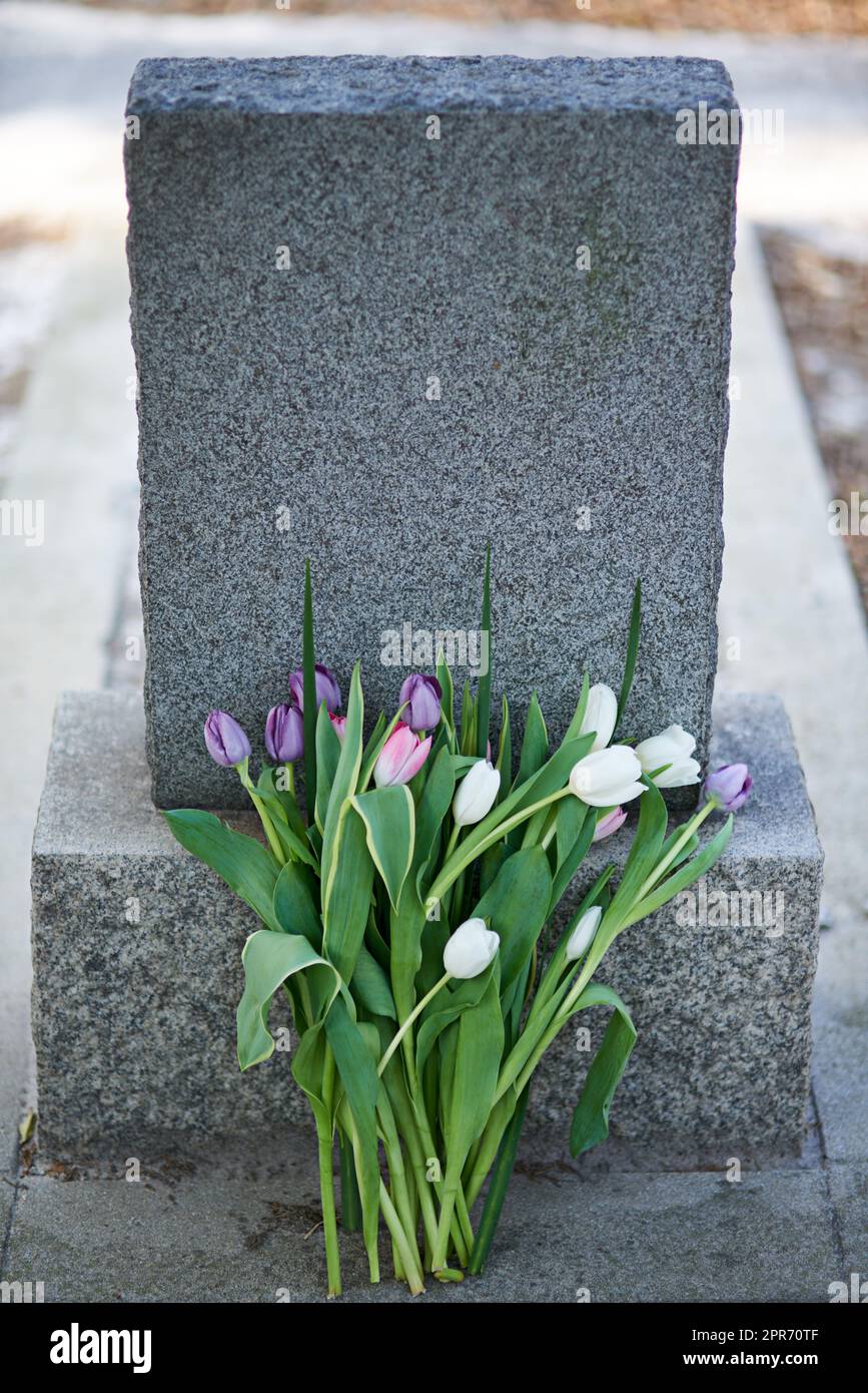 Flowers for the dearly departed. Shot of a gravestone in a cemetery. Stock Photo