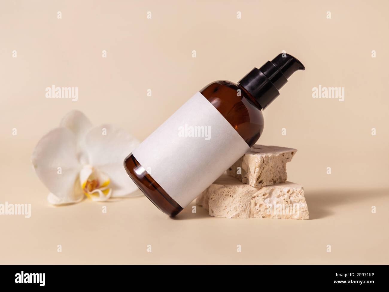 Brown glass cosmetic bottle near white orchid flower and stones on light yellow. Mockup Stock Photo