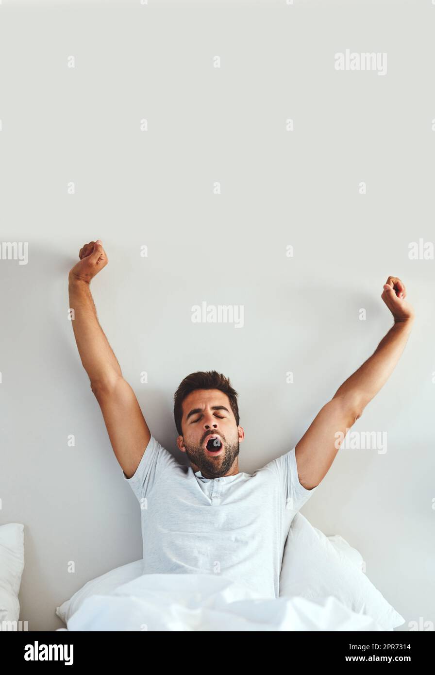 What a great nights sleep. Cropped shot of a tired young man stretching and yawning after waking up from a good nights sleep. Stock Photo