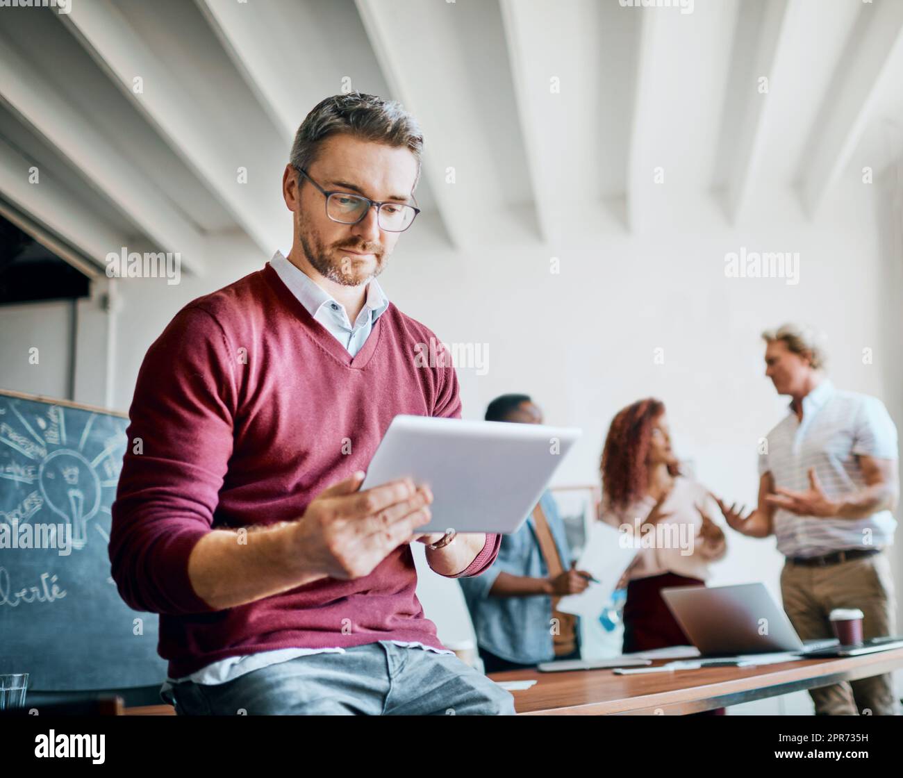 We have some work to do. Shot of a mature businessman working on his tablet while being seated in the office. Stock Photo