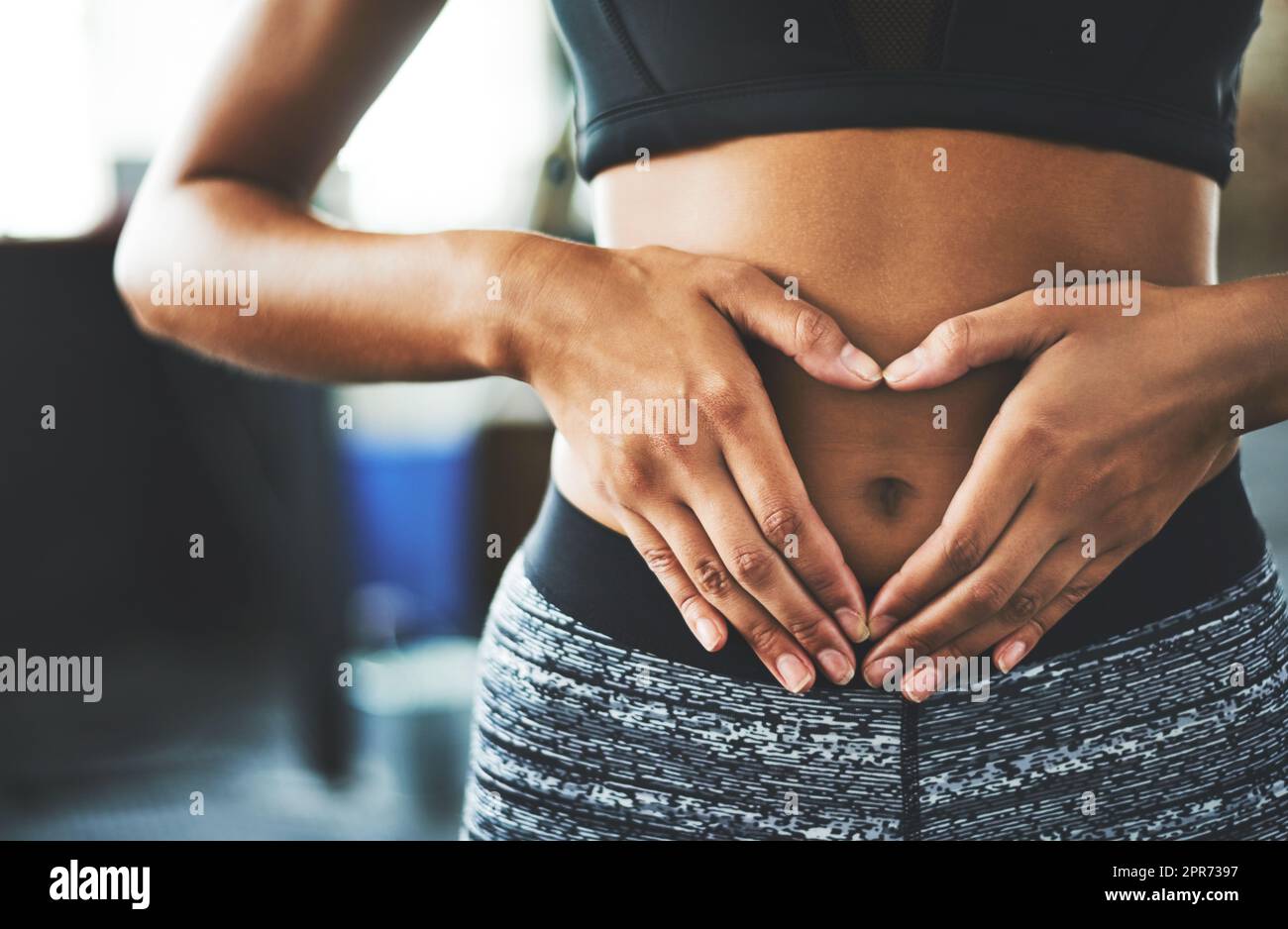 Everyday is core strengthening day. Cropped shot of a fit young woman making a heart shaped gesture over her stomach in a gym. Stock Photo