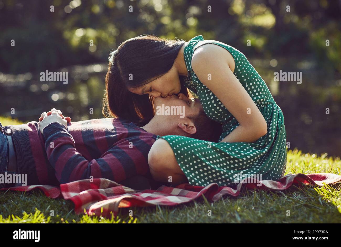 Nothing says romance like a picnic in the park. Shot of an affectionate young couple relaxing together on a picnic blanket in the park. Stock Photo