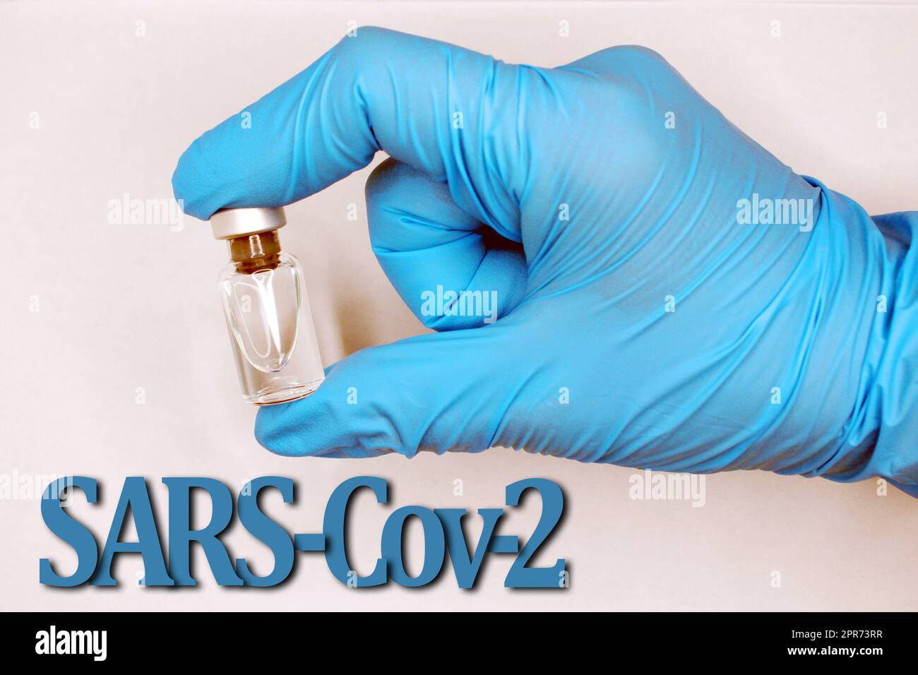 A hand in a blue medical glove close-up with a vaccine. SARS-Cov-2 inscription at the bottom. Stock Photo