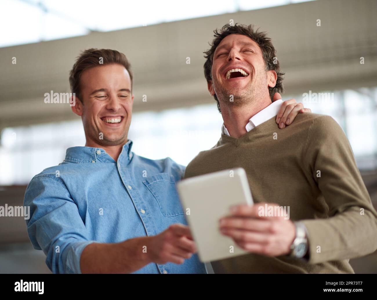 Take time out for a good old laugh. Male coworkers laughing out loud about something humorous on a digital tablet in their office. Stock Photo