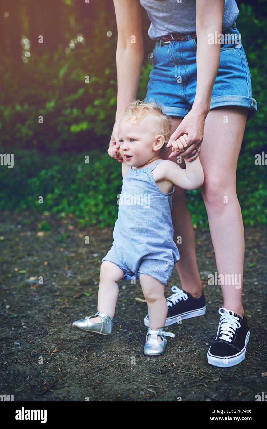 Today she walks, tomorrow she runs. Shot of an adorable baby girl learning to walk with help from her mother outdoors. Stock Photo