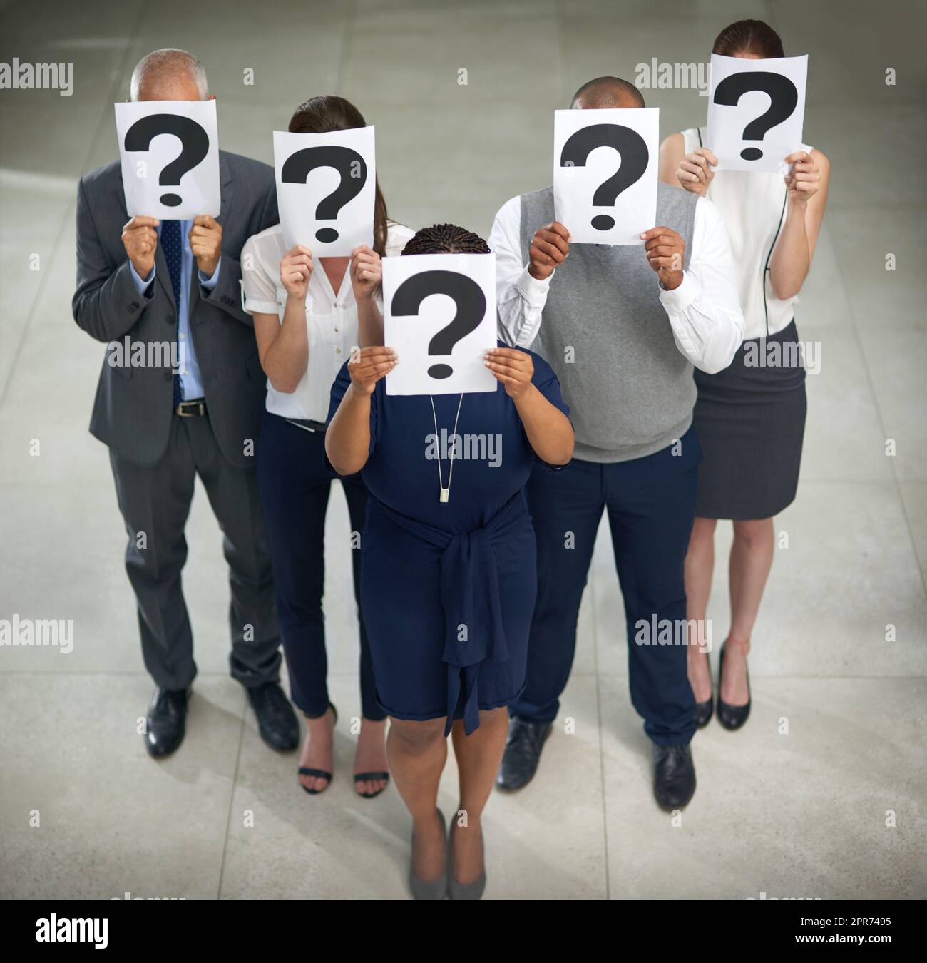 The secretive side of business. High angle shot of a group of businesspeople holding questions marks in front of their faces. Stock Photo