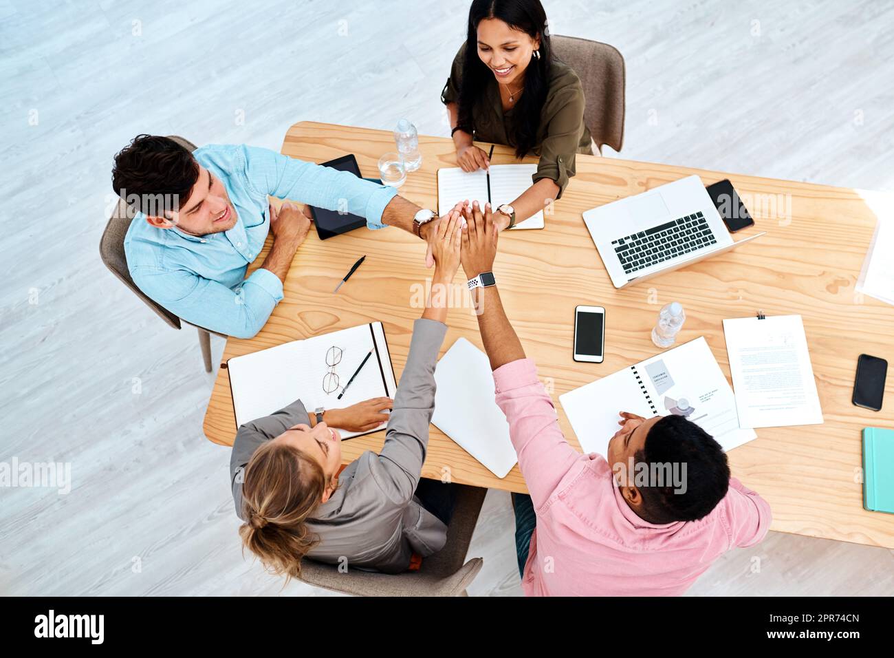 Inspired teams perform the best. High angle shot of a group of businesspeople giving each other a high five while working in an office. Stock Photo