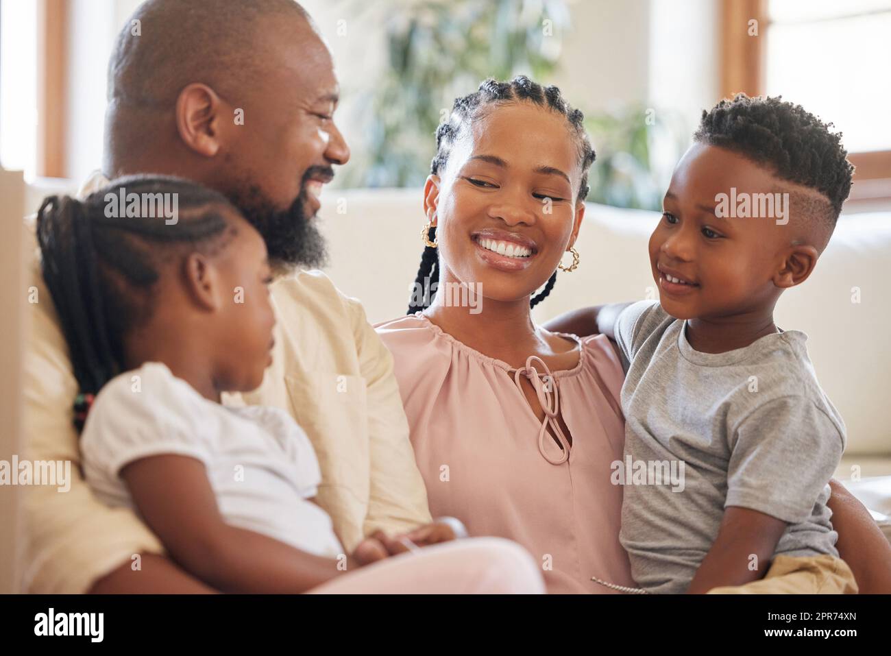 Relaxed african american family smiling while sitting on the couch. Shot of a young happy black couple relaxing on the sofa while talking to their two young adorable kids at home Stock Photo